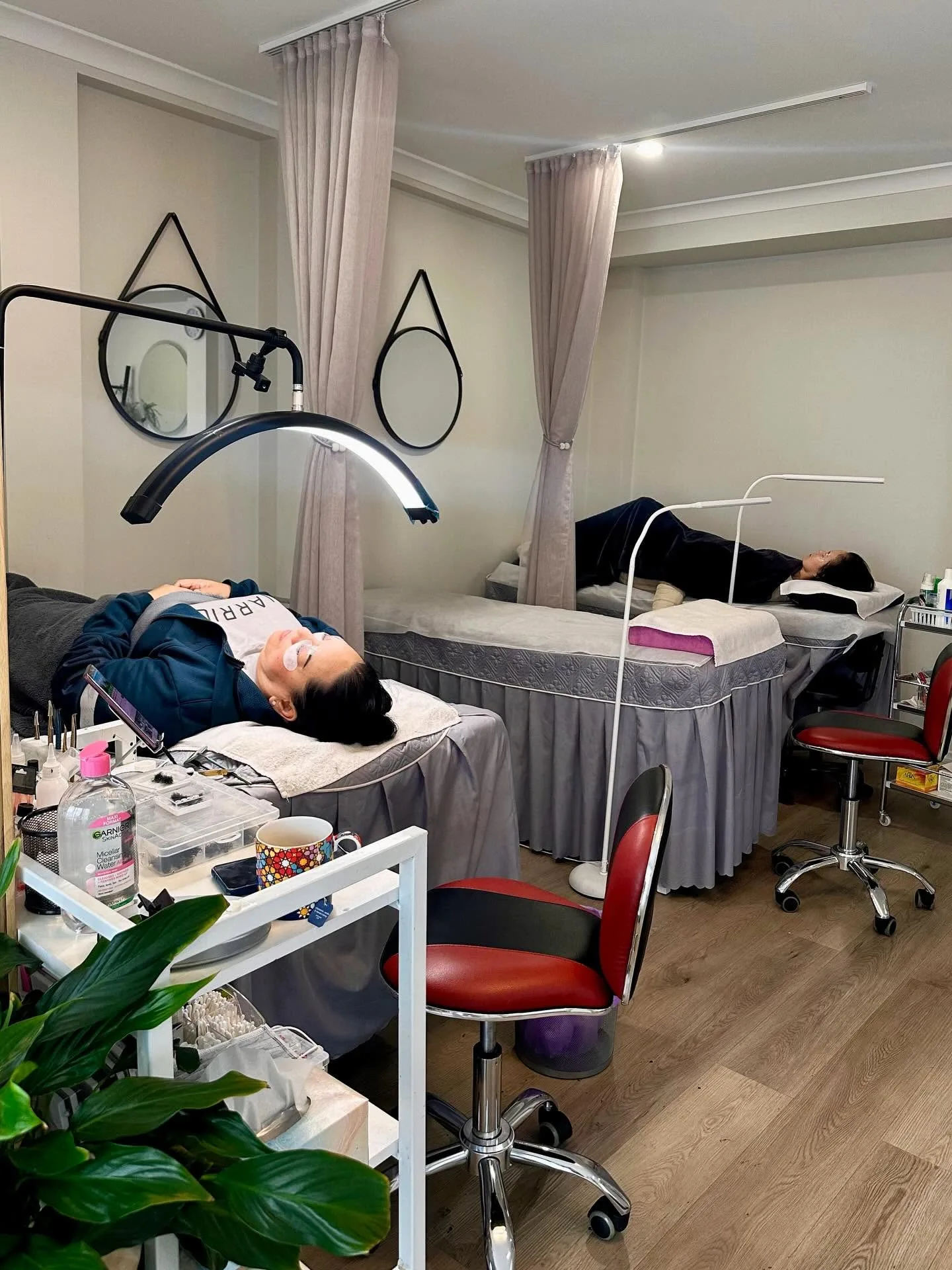 Tiffany's treatment room — two clients reclining for lash work beside round mirrors